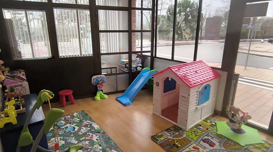Patio interior acristalado con tobogán azul, casita de juegos y alfombras de carreteras